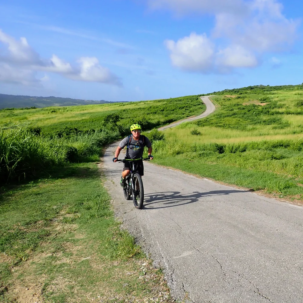 A cyclist riding a winding road through open Barbados countryside