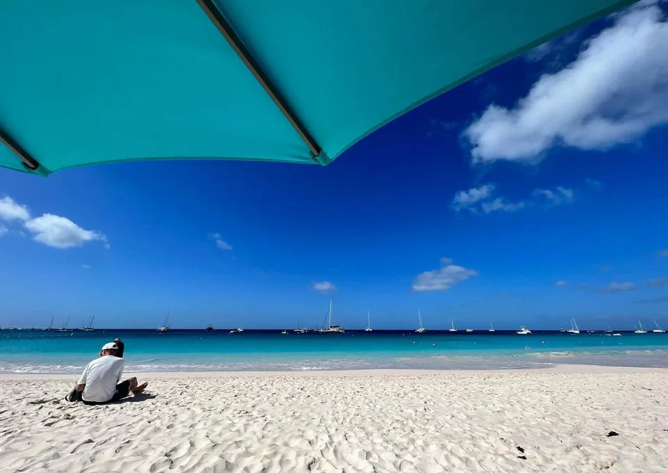 White sand and turquoise Carlisle Bay beneath a beach umbrella at Savvy On The Bay